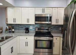 a kitchen with white cabinets and a stainless steel refrigerator at Cypress Cove Waterfront Townhome with Boat Ramp in Inverness