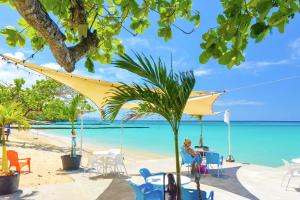 Eine Frau, die an einem Tisch am Strand sitzt. in der Unterkunft Sand and Tan Beach Hotel in Ocho Rios