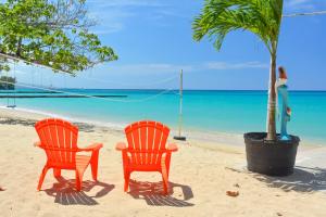 two chairs and a palm tree on a beach at Sand and Tan Beach Hotel in Ocho Rios
