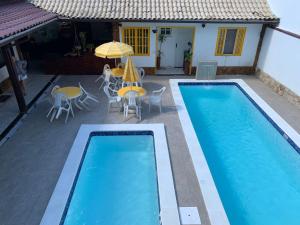 una piscina con sillas, una sombrilla y una casa en Pousada Fazendinha Unamar en Cabo Frío
