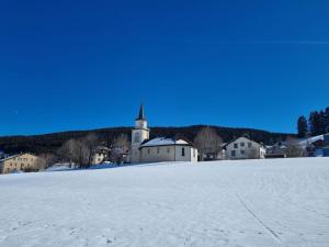 a large field of snow with a church in the background at Appartement chaleureux et confortable avec sauna.. in Le Chenit
