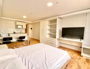 a white bedroom with a large bed and a flat screen tv at Loft Executivo-Afonso Pena in Campo Grande