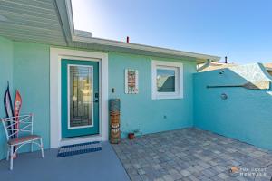 uma casa azul com uma cadeira e uma porta em Relaxing Beach Home with Fire Pit and Private Fenced Yard STEPS from the Sand! em New Smyrna Beach
