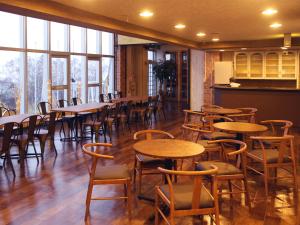 uma sala de jantar com mesas, cadeiras e janelas em Shiga Swiss Inn em Yamanouchi