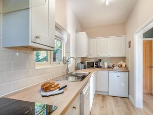 uma cozinha com armários brancos e um lavatório em Brickyard Cottage em Metheringham