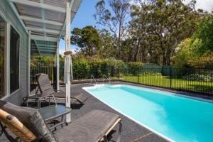 a swimming pool with chairs and a table and an umbrella at Grey Gables Pet Friendly with Swimming Pool and Spa in Callala Bay