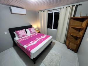 um quarto com uma cama com lençóis cor-de-rosa e uma janela em Maddy's House em Maatea