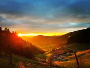 um pôr-do-sol nas montanhas com uma casa numa colina em Ferienhaus Wendelinus mit Pool & Sauna em Hausach