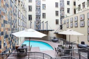 a swimming pool with tables and umbrellas in front of a building at Lovely 2 Storey apartment with pool, gym and bar in Johannesburg