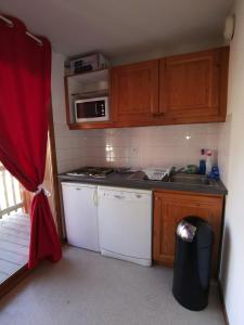 - une petite cuisine avec des appareils blancs et un rideau rouge dans l'établissement Appartement cosy dans chalet vue Montagne, à Saint-Étienne-en-Dévoluy