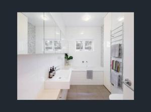 uma casa de banho branca com uma banheira e um lavatório em Modern Queens Park Home near Bondi Junction, Bondi Beach & City em Sydney