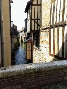 eine schmale Gasse mit Gebäuden und eine Straße mit Wasser in der Unterkunft Belle demeure Normande dans son écrin de verdure. in Manneville-sur-Risle