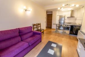 a living room with a purple couch and a kitchen at Apartamentos & casas rurales Santo Domingo de Silos in Santo Domingo de Silos