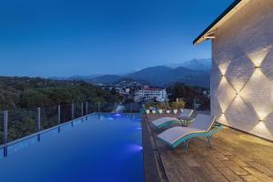 a swimming pool with chairs and a view of the mountains at INFINITEA CENTRIC DHARAMSHALA in Dharamshala