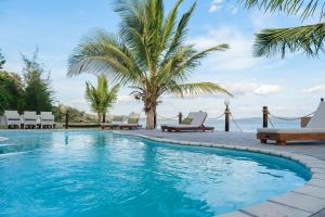 a swimming pool with chairs and a palm tree at Mukumbura Lodge Bilene in Vila Praia Do Bilene