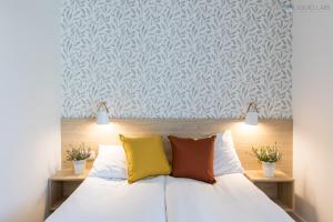 um quarto com uma cama com lençóis brancos e almofadas coloridas em Ośrodek Turystyczny Warzenko em Warzenko