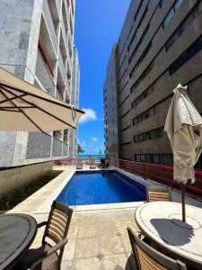 a swimming pool with a table and an umbrella at Navegantes apartamento in Recife