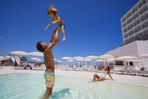 a man and a child jumping into a swimming pool at Palladium Hotel Menorca in Arenal d'en Castell