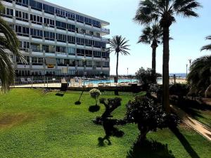 a large building with palm trees in front of a park at Newly refurbished beachfront apartment. in San Bartolomé de Tirajana