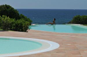 a woman sitting in a swimming pool next to the ocean at Hotel Punta Negra in Alghero