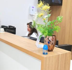 a vase of flowers on a desk with a woman at VR2 Hotel in Lençóis Paulista