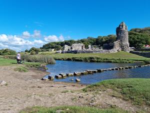 a person sitting on a bench next to a river with a castle at Driftmark Aberavon Beach The Crownlands 4 bedrooms Large Driveway parking 2 mins from Beach in Port Talbot