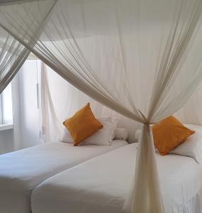 - une chambre dotée d'un lit à baldaquin avec des draps blancs et des oreillers orange dans l'établissement Trancoso Terravista Villa Floresta, à Trancoso