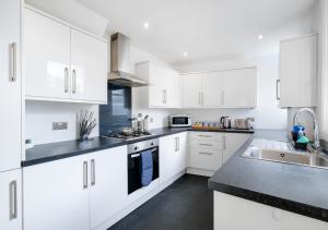 una cocina blanca con armarios blancos y fregadero en Lovely 4 Bedroom London Home with Free Parking, Garden, WiFi By Roost Accommodation, en Kingston upon Thames