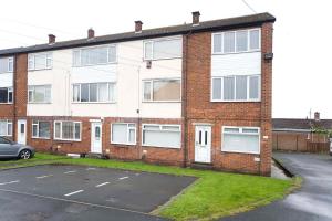 a brick building with a car parked in a parking lot at Belmont Budget Apartment in Stockton-on-Tees