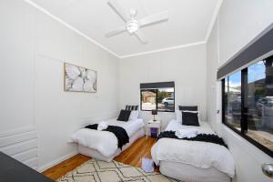 2 camas en una habitación con paredes y ventanas blancas en Large Cottage Near Ettalong Centre en Ettalong Beach