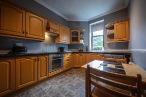 cocina con armarios de madera, mesa y ventana en Jardine Apartment @ Cairn Dhu House en Stornoway