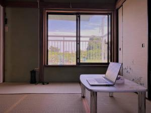 湘南の潮風に吹かれて自然豊かな丘ーーー湘南の丘のヴィラ＠ふじさわ في فوجيساوا: وجود الكمبيوتر المحمول على طاولة أمام النافذة