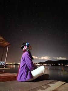 una mujer sentada en un muelle mirando el agua por la noche en Uros Walysuma Titicaca Lodge en Puno