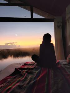 a woman sitting on a bed looking at the sunset at Uros Walysuma Titicaca Lodge in Puno
