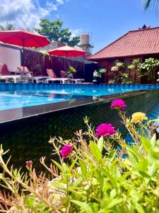 a swimming pool with pink flowers in the foreground at Lembongan Tropical Guesthouse in Nusa Lembongan