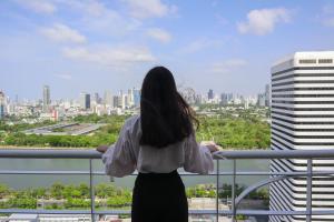 Eine Frau steht auf einem Balkon mit Blick auf die Stadt in der Unterkunft Shama Lakeview Asoke Bangkok in Bangkok