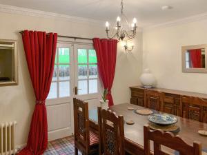 a dining room with a table and red curtains at Sluice Keepers Cottage in Skelbo