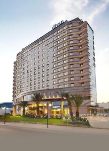 a large hotel building with palm trees in front of it at Divan Mersin in Mersin