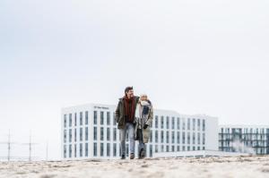 Ein Mann und eine Frau stehen am Strand mit Gebäuden im Hintergrund in der Unterkunft aja Travemünde in Travemünde