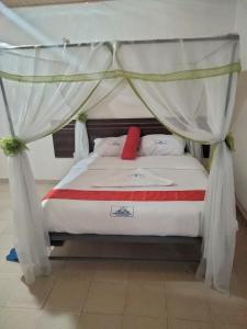 ein Bett mit einem Baldachin und einem roten Kissen darauf in der Unterkunft Good Morning Hotel Rongo in Paulo