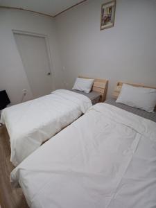two beds in a room with white sheets at J&J Guesthouse in Jeonju