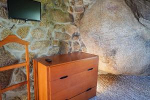 a wooden dresser with a tv on a stone wall at O Refúgio da Serra do Caramulo in Caramulo