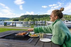 a woman sitting at a picnic table eating food on a grill at Topcamp Mjøsa - Brumunddal in Brumunddalen