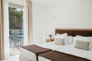 a bedroom with a large white bed and a balcony at Porto Drach Aparthotel & Suites in Porto Cristo