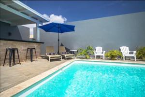 a swimming pool with chairs and an umbrella at Bida Marino Residence Aruba in Palm-Eagle Beach