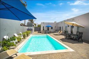 Bida Marino Residence Aruba في شاطئ بالم إيغل: مسبح مع كراسي ومظلات بجوار منزل