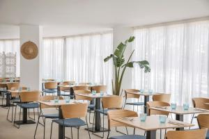 a dining room with tables and chairs and windows at Porto Drach Aparthotel & Suites in Porto Cristo