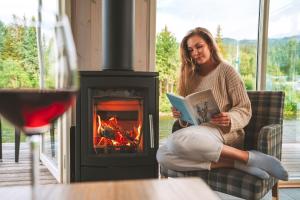 a woman sitting on a couch reading a book in front of a fireplace at Topcamp Hallingdal - Ål in Al