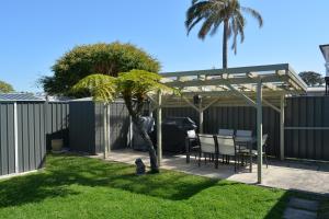 un patio trasero con pérgola, mesa y palmera en Baltica Beach House, en Culburra Beach