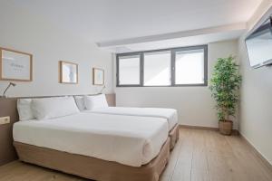 a white bedroom with a large bed and a window at Aparthotel Bcn Montjuic in Barcelona
